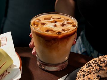 Iced coffee in a glass held by a person.