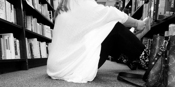 Person sitting on the floor in a bookstore, reading a book.