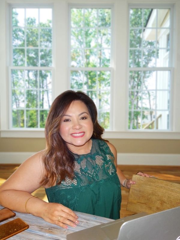 Smiling woman in a green lace top sitting at a table with a laptop.