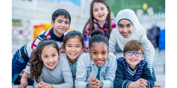 Group of 7 children of mixed ethnic backgrounds laying on the floor forming a pyramid. 