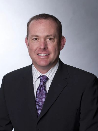 Professional man in a suit with a patterned purple tie smiles at the camera.
