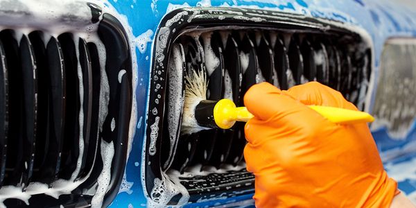 Blue BMW Grille being detailed with a soft brush while covered in foam.
