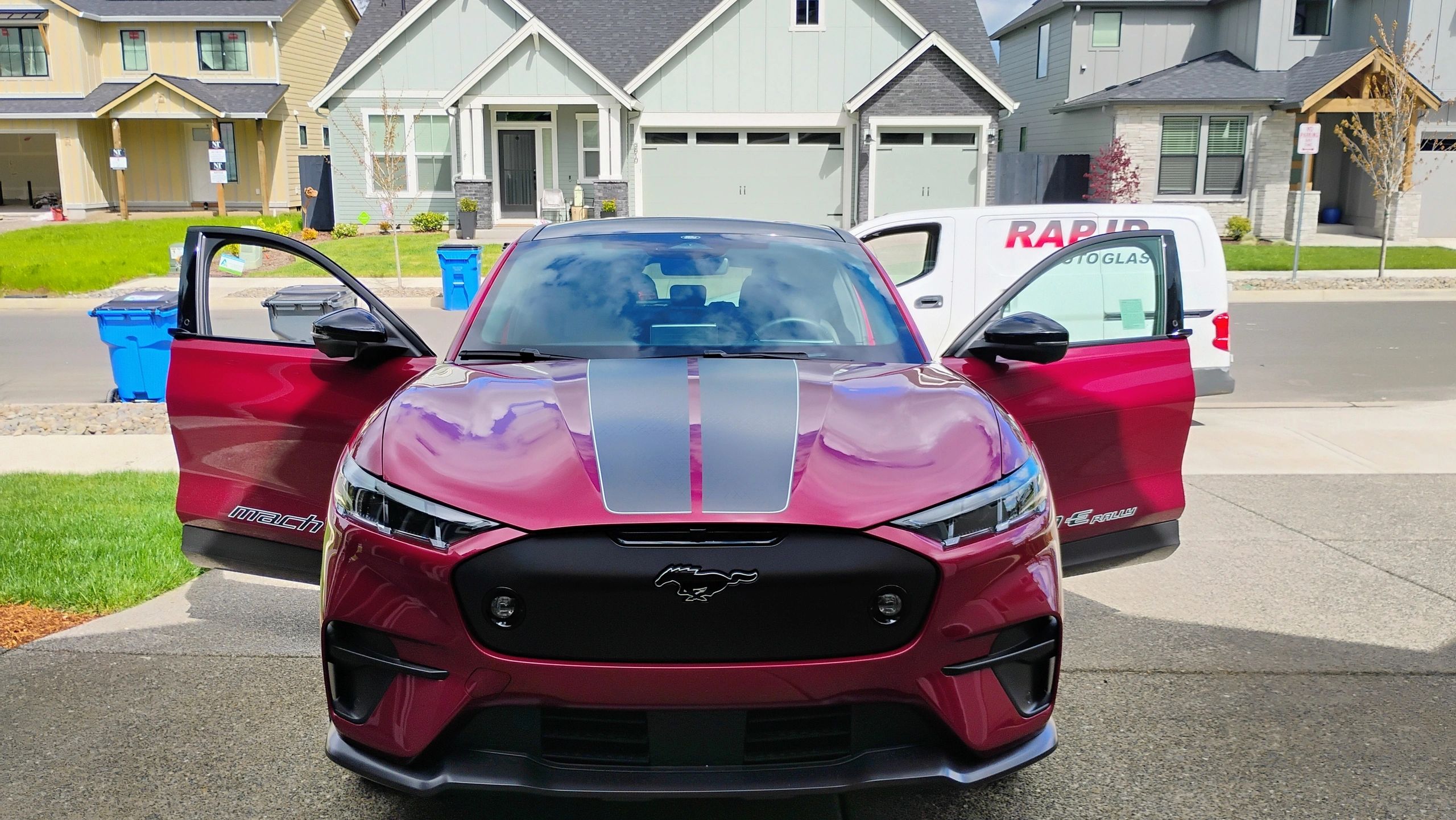 Front view of a red Mustang Mach-E with open doors in a suburban driveway.