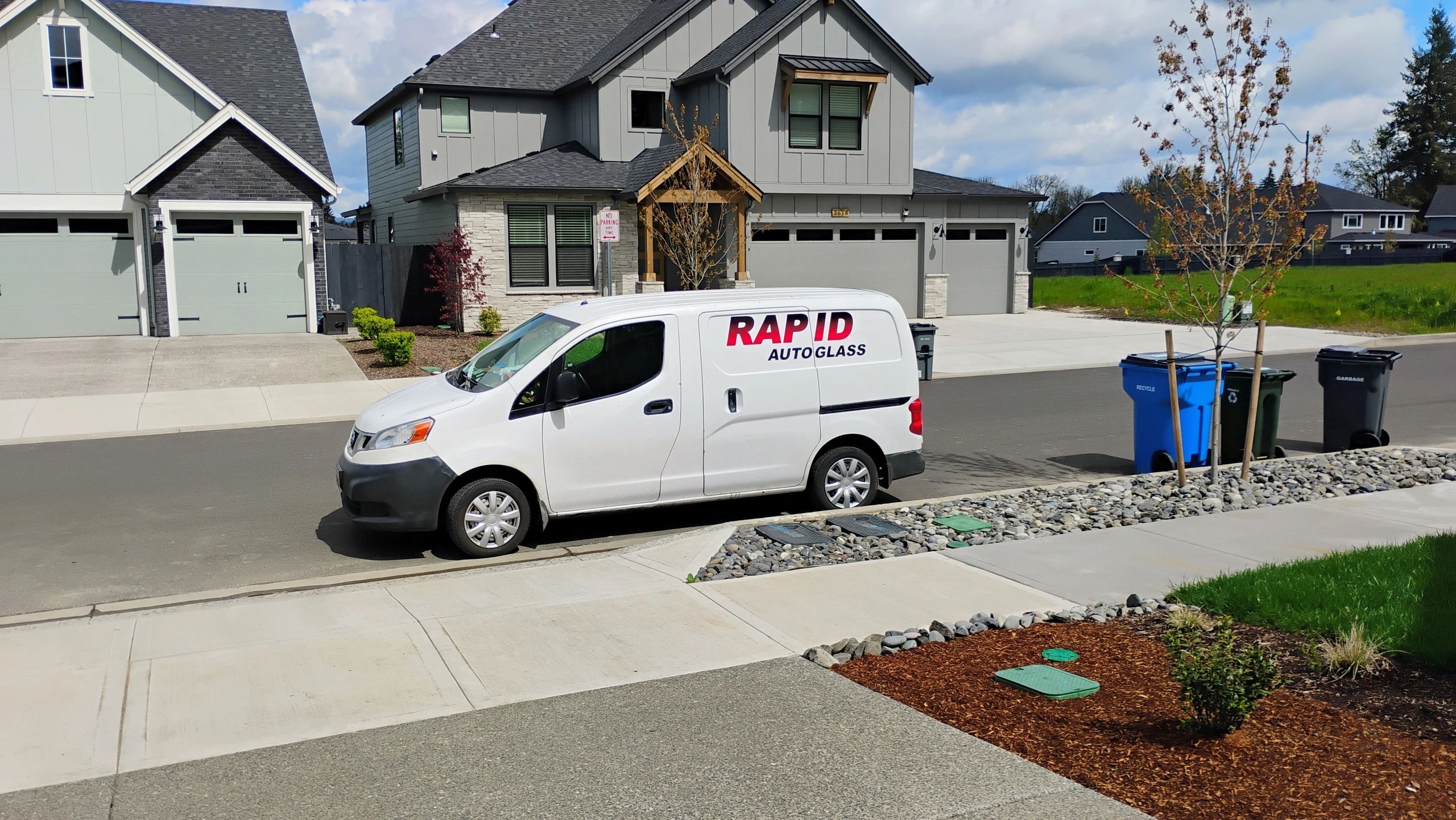 White Rapid Auto Glass van parked on a suburban street in front of modern houses.