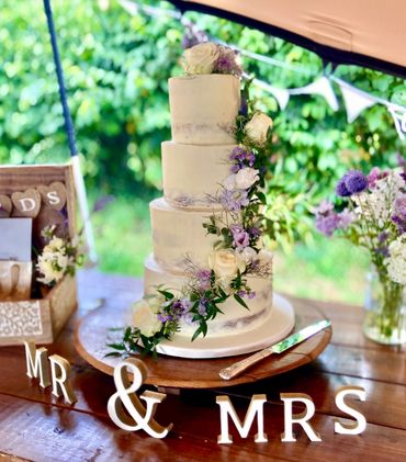 Semi naked wedding cake with a cascade of purple and white flowers 