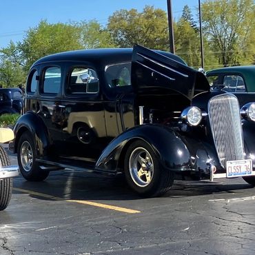 A classic black vintage car with hood open.