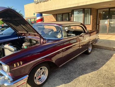 Classic maroon car with hood open in front of building.