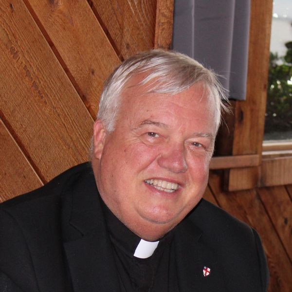 Smiling elderly priest in black clerical attire.