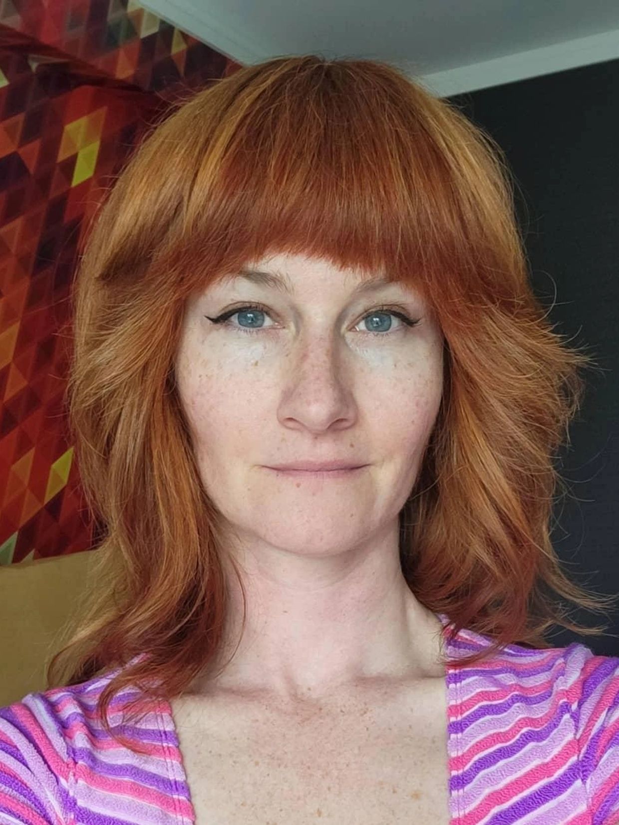 Woman with red hair and blue eyes wearing a striped top.