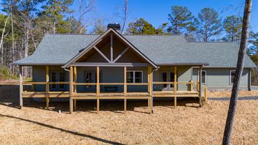 A green custom ranch house built for accessibility with large covered porches and a 2 car garage