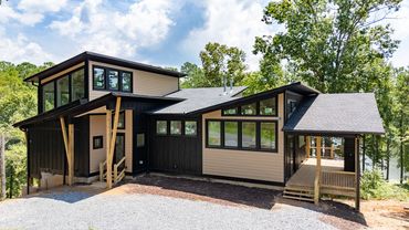 A large custom modern home with covered porches and big windows on a sloped lot on a small lake