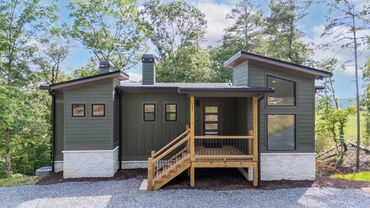 A forest green custom modern house with a covered front porch, white stone accent and big windows