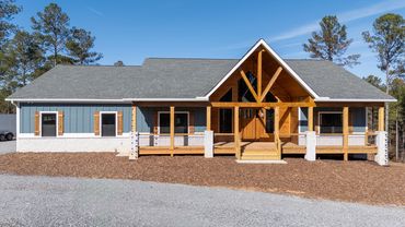 A blue single story custom ranch house with a covered front porch and white stone and wood entryway
