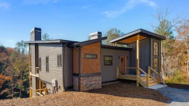 A custom modern house built on a slope with large covered porches, stone accents and cedar shake