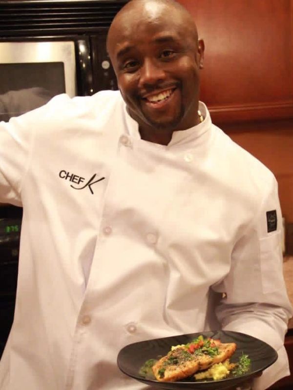Smiling chef presenting a beautifully plated fish dish.