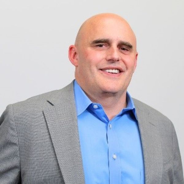 Smiling bald man in a blue shirt and gray suit jacket.