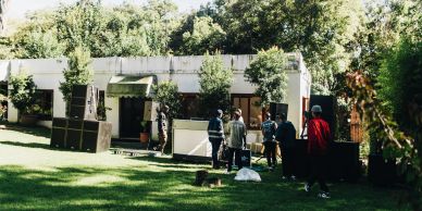 People setting up speakers and equipment outside a building on a grassy lawn.