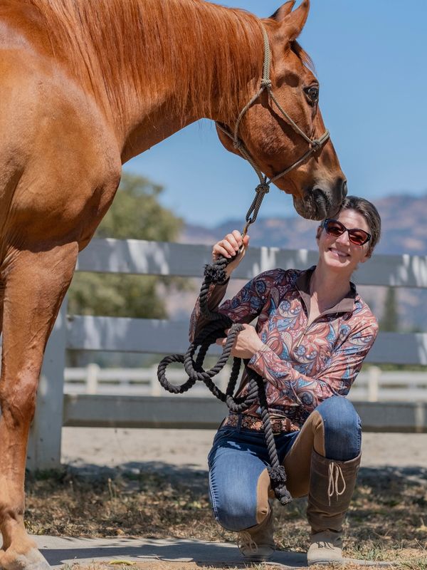 Person kneeling beside a horse outdoors, holding its lead rope.