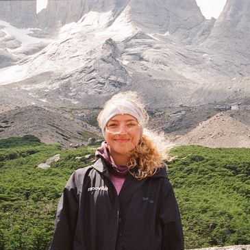 Smiling woman in outdoor gear with rocky mountain backdrop.