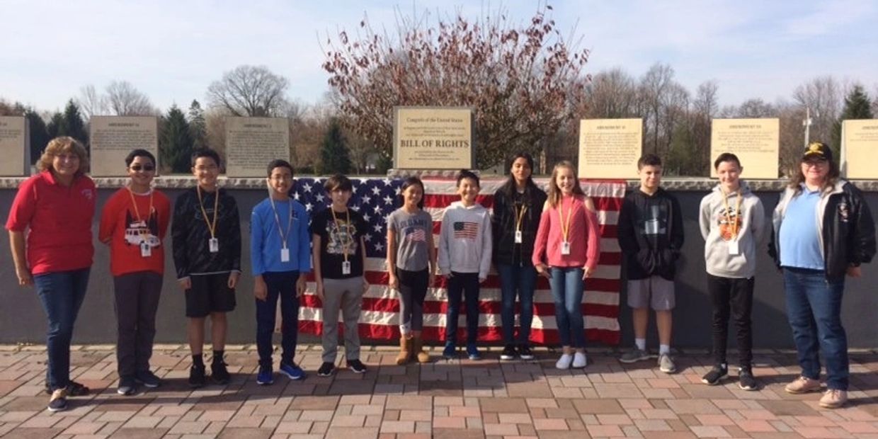 Group of students and teachers standing in front of a Bill of Rights monument with an American flag.