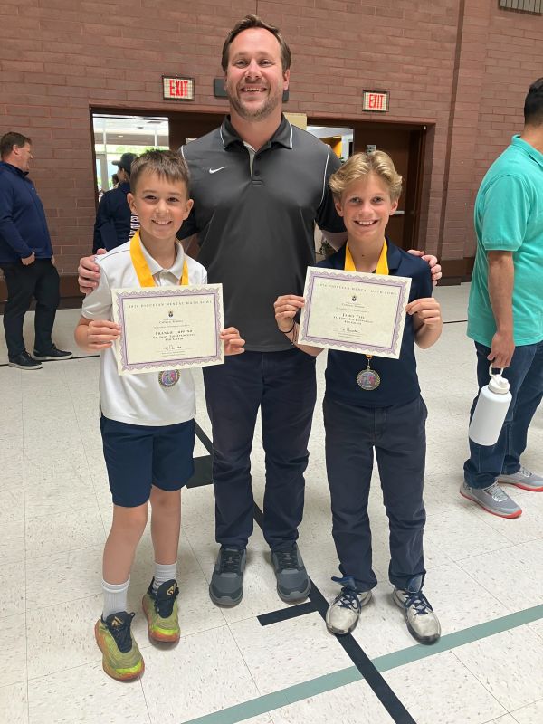 Two boys with medals and certificates standing with a smiling man.