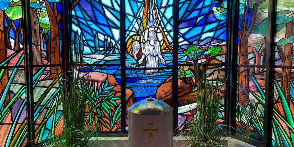 Stained glass window with religious scene and plants.