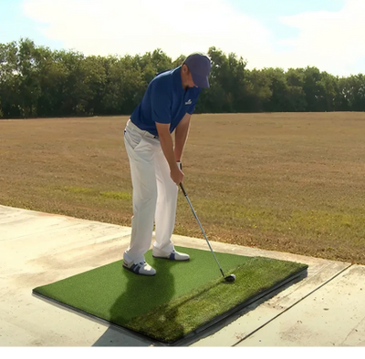 Man preparing to hit a golf ball on an artificial turf mat.