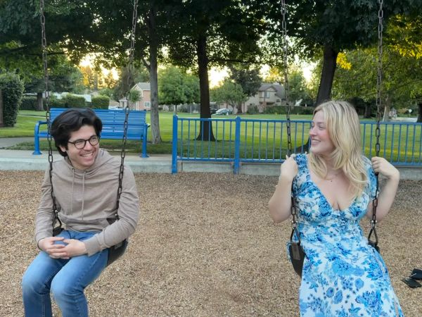 Two people smiling on swings in a park.