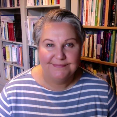 Smiling woman in striped shirt with bookshelves in background.