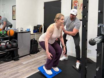 Elderly woman exercising with trainer's help in a gym.