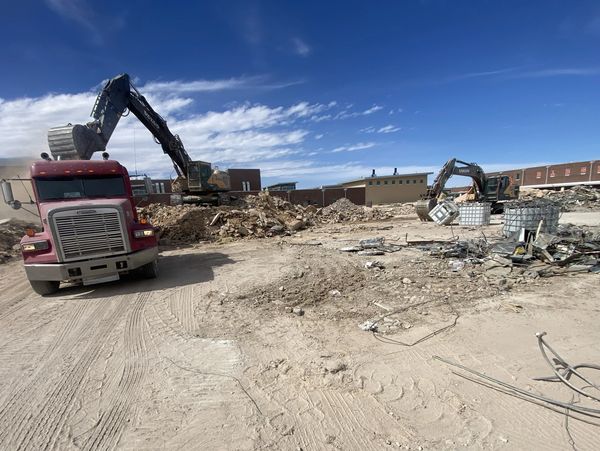 Excavators loading debris into a red dump truck on a sunny construction site.