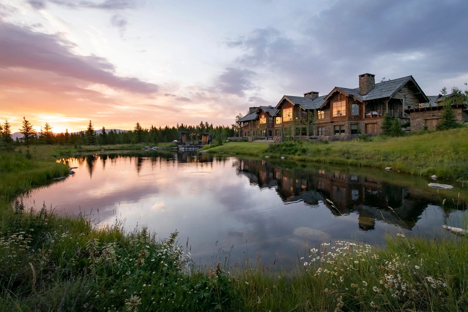 Large rustic house by a peaceful pond at sunset.
