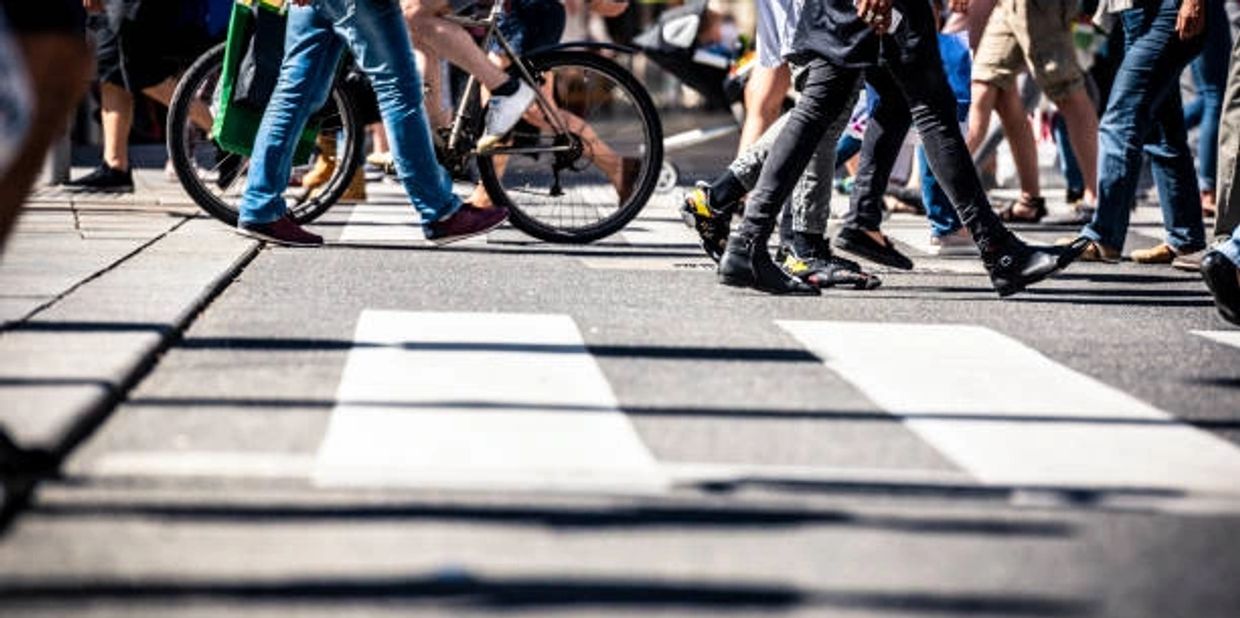 People walking across a busy city crosswalk with a bicycle.