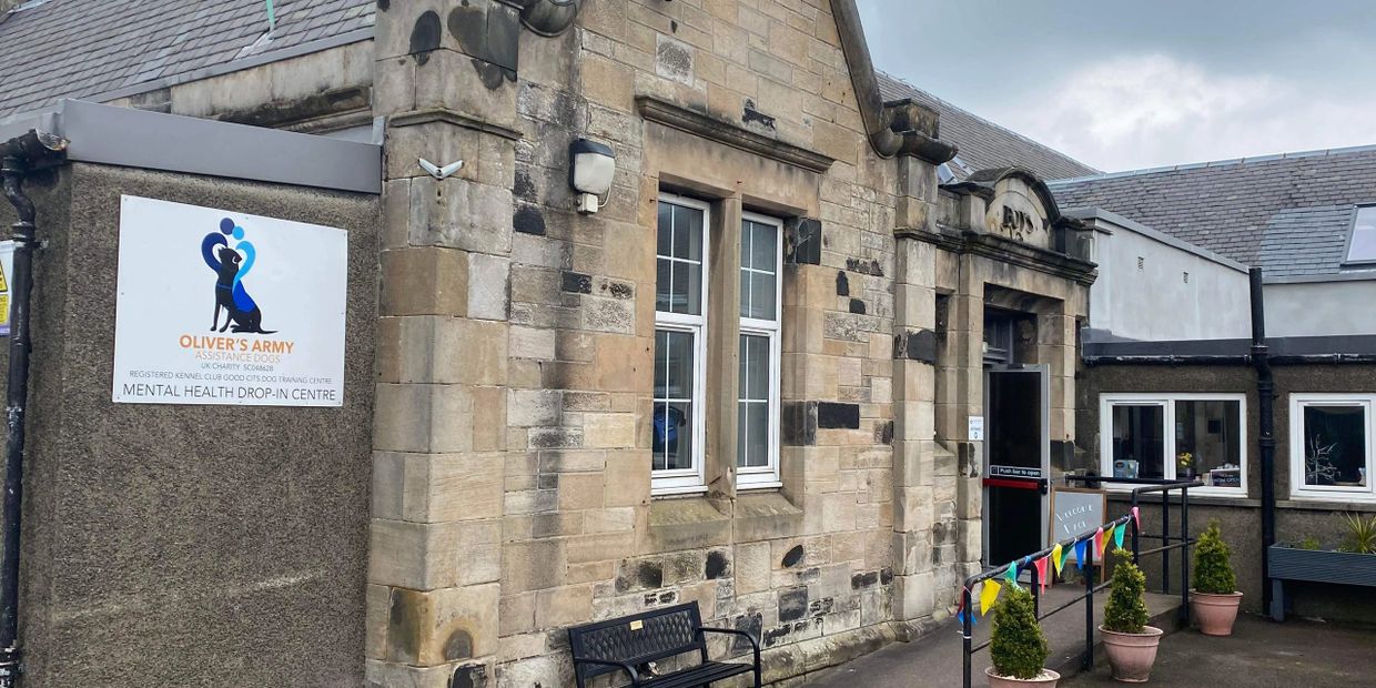 Old stone building housing a mental health drop-in centre with a bench and potted plants outside.