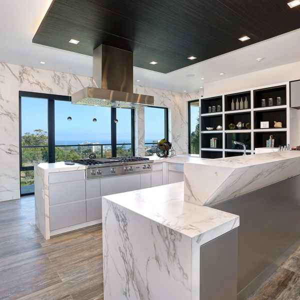 Modern kitchen with marble countertops and large windows showcasing a scenic view.