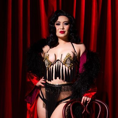 Woman in glamorous burlesque outfit with red curtains background.