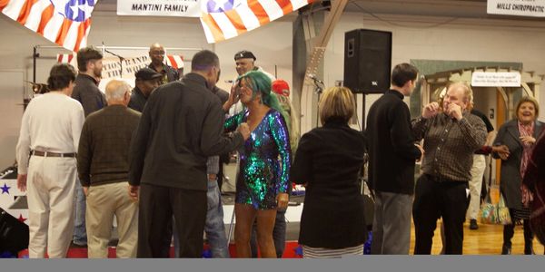 People gather and chat at an indoor event with patriotic decorations.