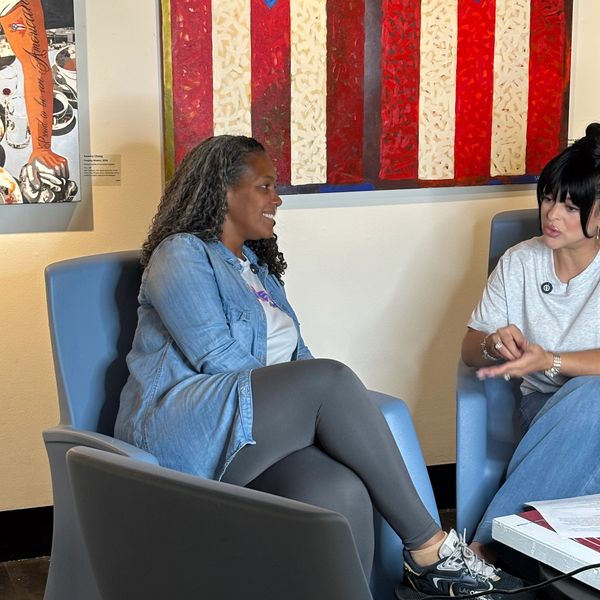 Two women engaged in a conversation in a room with Puerto Rican flag artwork.