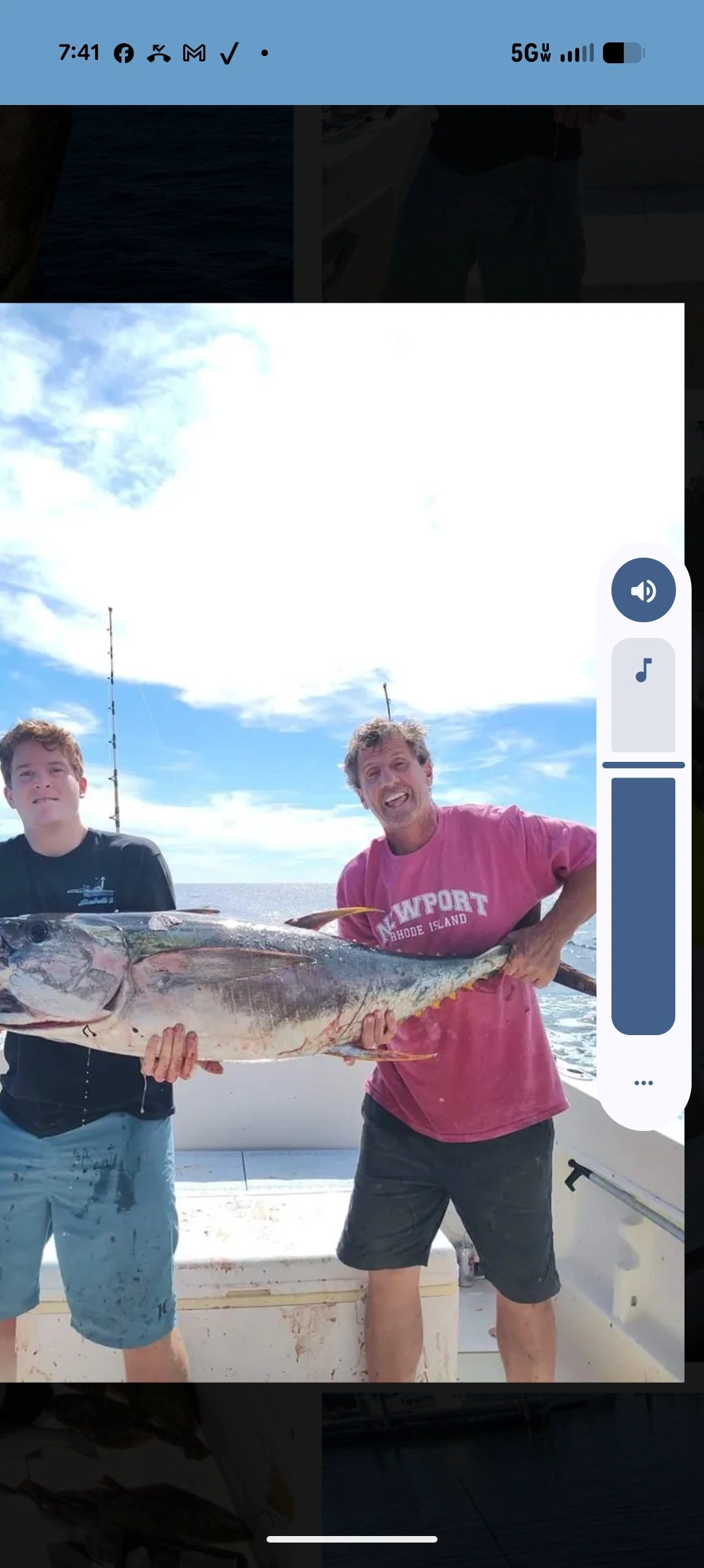 Two men on a boat holding a large fish.
