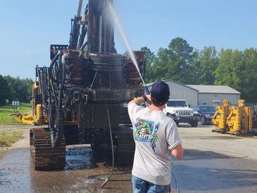 Man pressure washing large construction equipment outdoors.