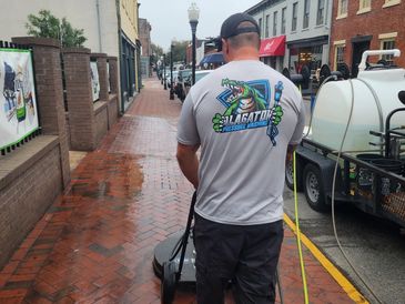 Man pressure washing a brick sidewalk on a rainy day.