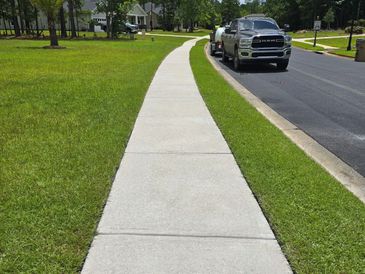 A clean sidewalk winds through a green suburban neighborhood under a partly cloudy sky.