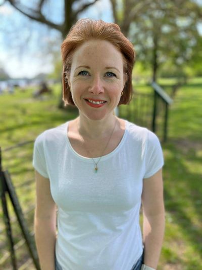 Woman with short, red hair smiling in the sunshine in a park