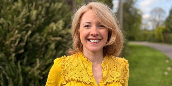Smiling woman in a bright yellow blouse outdoors on a sunny day.
