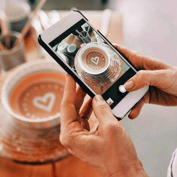 Person photographing a coffee cup with heart-shaped latte art on a smartphone.