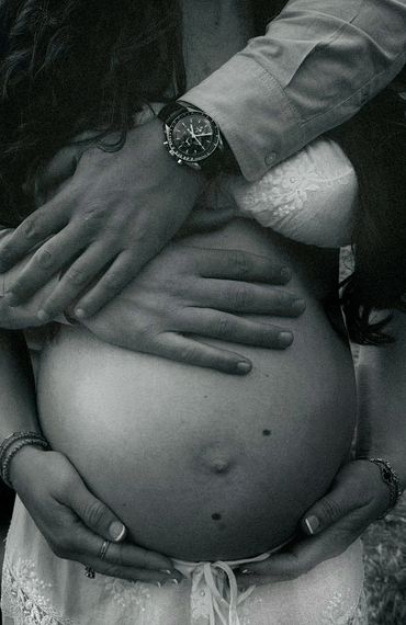 Couple's hands gently embracing a pregnant belly in black and white.