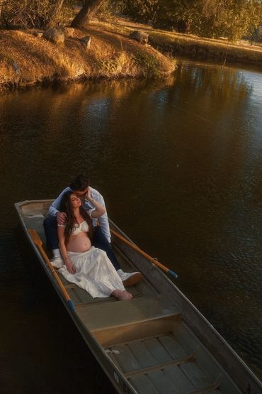 Couple sharing a tender moment in a boat on a river during golden hour.