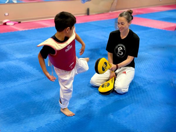 Child practicing a Taekwondo kick with an instructor at Douglas Martial Arts in Moose Jaw.