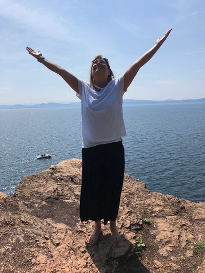 Suzanne standing on a rock with arms raised near the water