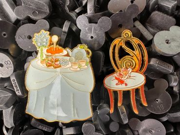 Two decorative pins featuring tea table and chair designs.